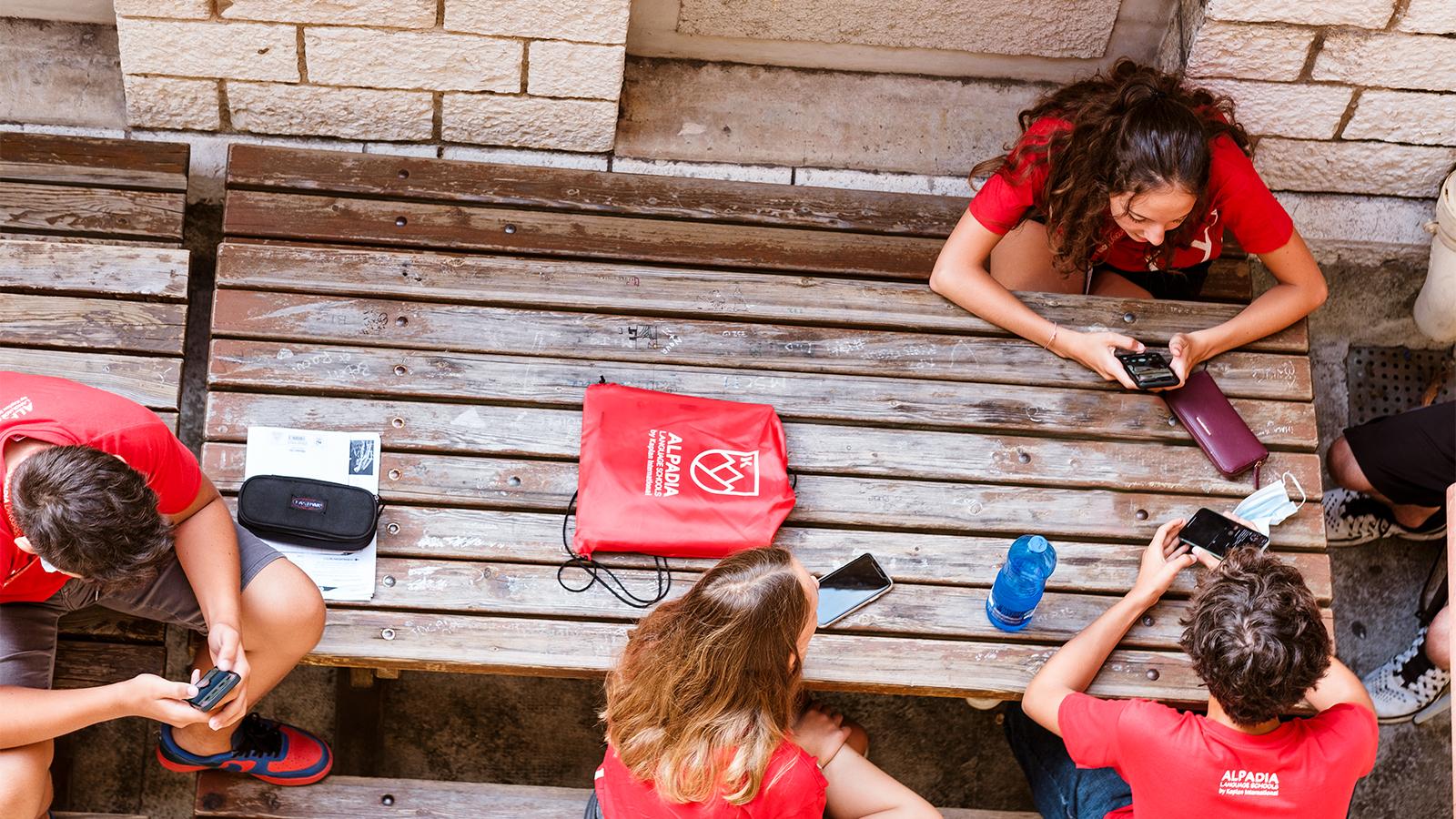 students looking seated at a wood table and looking at their phone